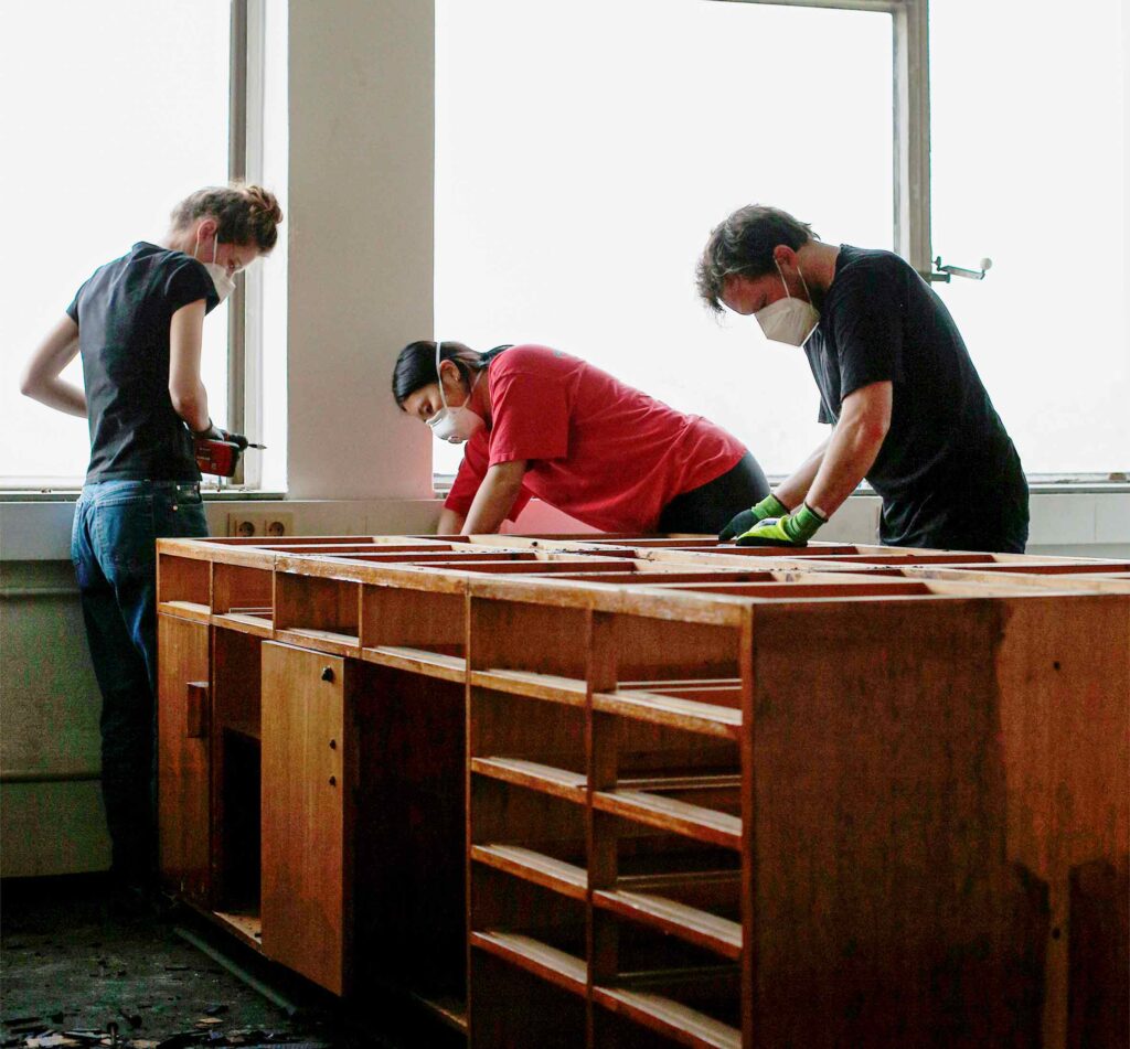 3 persons are working with different building materials on a wooden working bench
